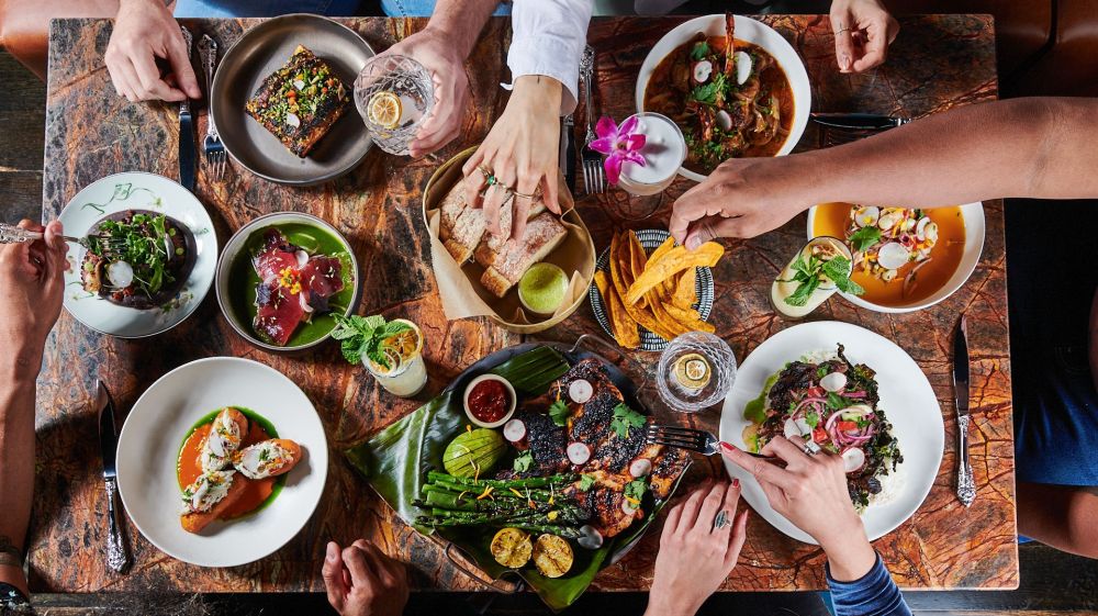 Hands excitedly reach over a spread of food at Little Bull in Durham, NC