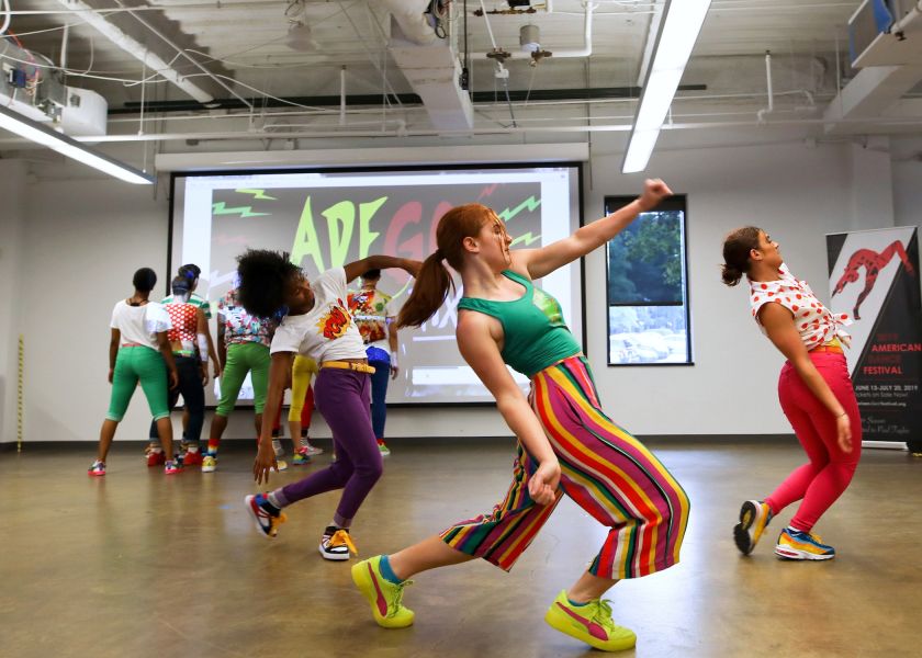 Performers in colorful clothing dance in a well-lit room at the American Dance Festival, Durham, NC.