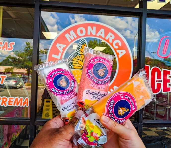 A customer holds up 3 frozen treats in front of the sign at La Monarca Michoacana in Durham, NC.