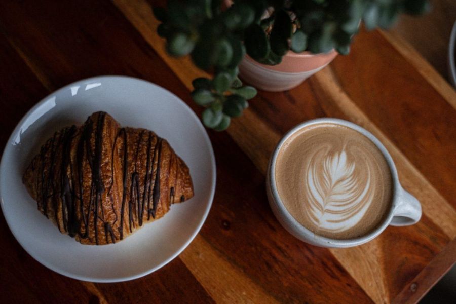 A croissant with chocolate drizzled on top sits on a wood table next to a latte at People's Coffee in Durham, NC.