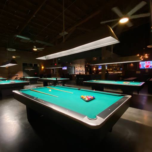 A dark room with six pool tables and a bar in the background.