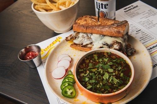 Birria french dip sandwich with a can of Miller Lite and fries at Queeny's in Durham, NC.