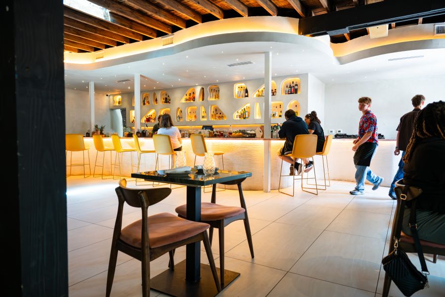Yellow lights shine over the soft white interior of Aaktun as customers enjoy drinks at the bar.