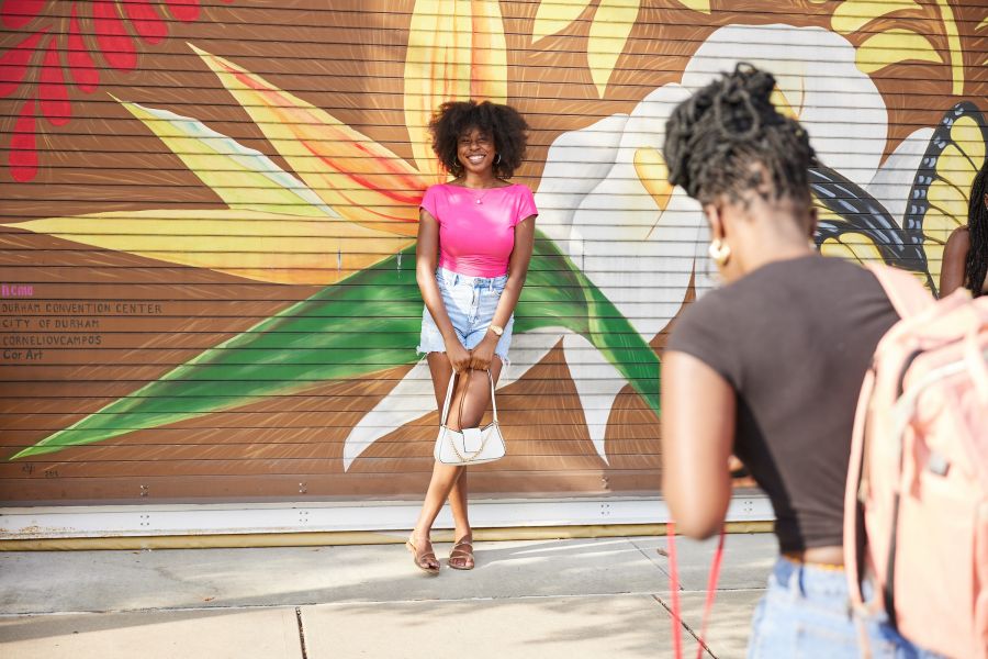A woman poses for the camera in front of a large mural in downtown Durham
