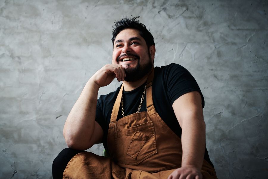 Chef Oscar Diaz smiles for the camera in front of a grey back drop.