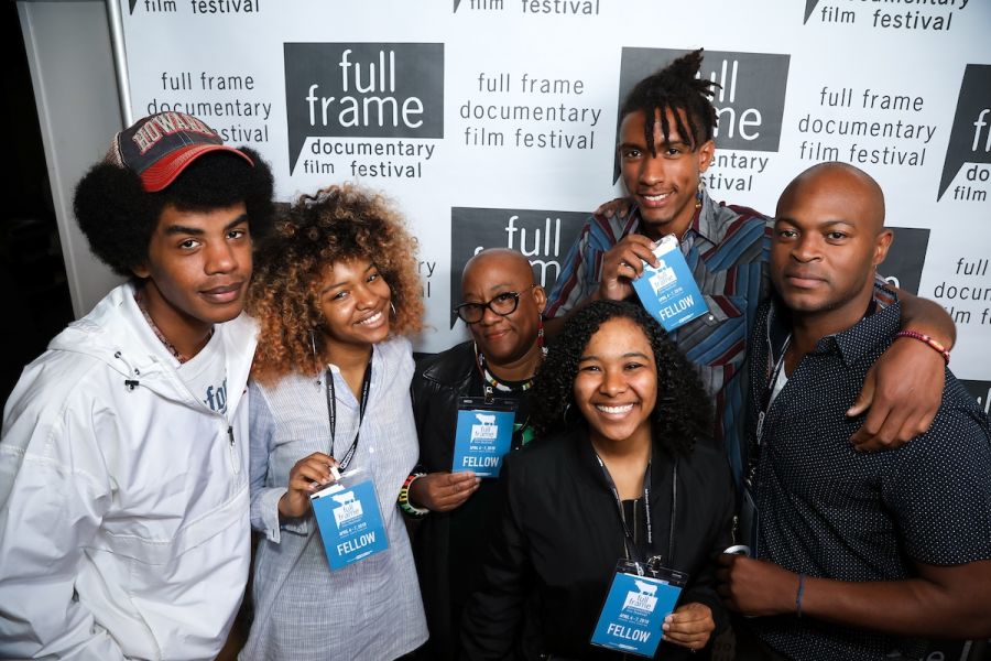 A group of fellows showing off their lanyards in front of a step and repeat for Full Frame Documentary Film Festival