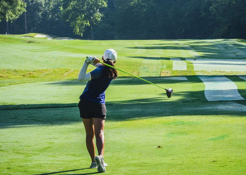 A golfer tees off on a serene course surrounded by trees.