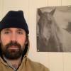 Writer and Musician Dylan Angell stands next to a black and white photo of a horse.