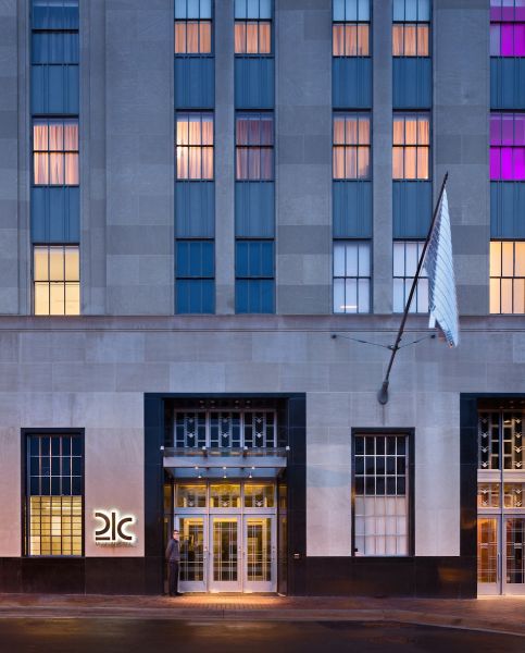 The exterior of the 21c hotel in downtown Durham. A flag flies to the right of the door; windows above lit with purple light.