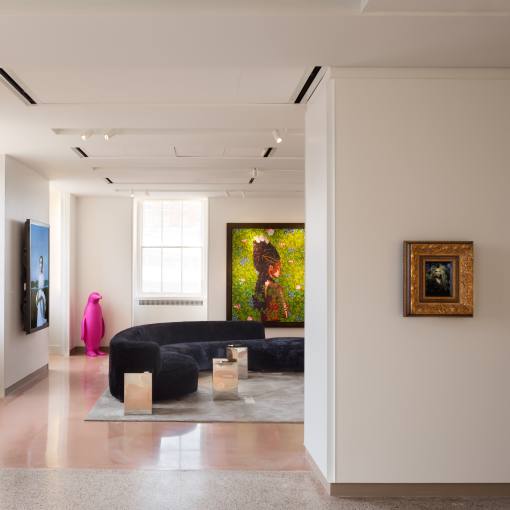 An art gallery with artwork on each wall and a column in the center of the room. A sofa sits on the floor in the middle.