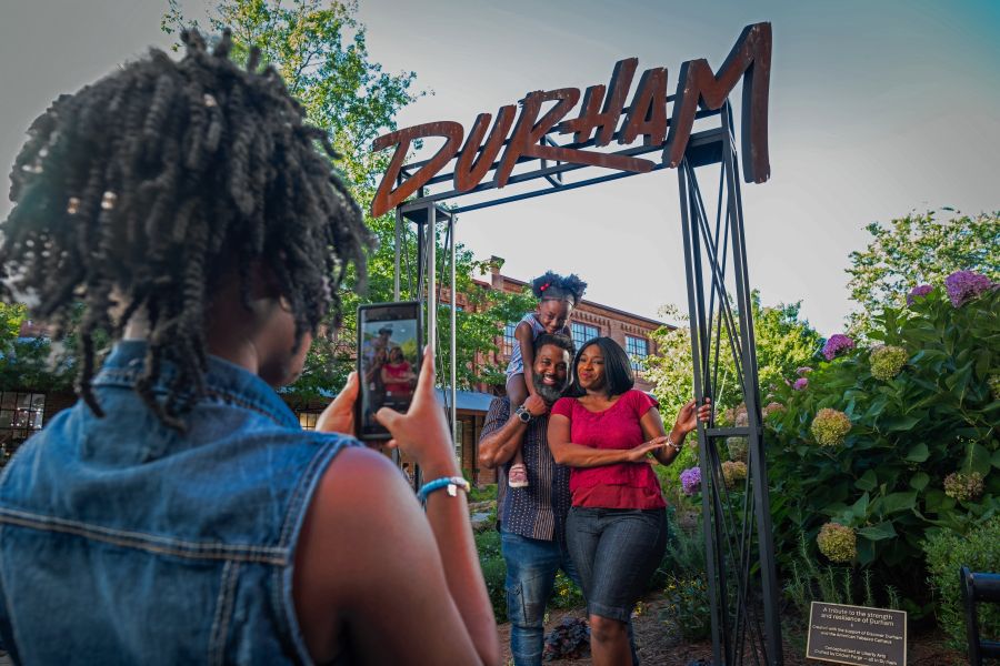 A husband, wife, and daughter pose for a photo in front of the Durham sign.