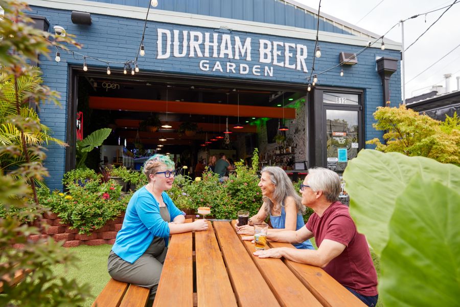 Three guests sit at a picnic table on the patio at The Durham Beer Garden