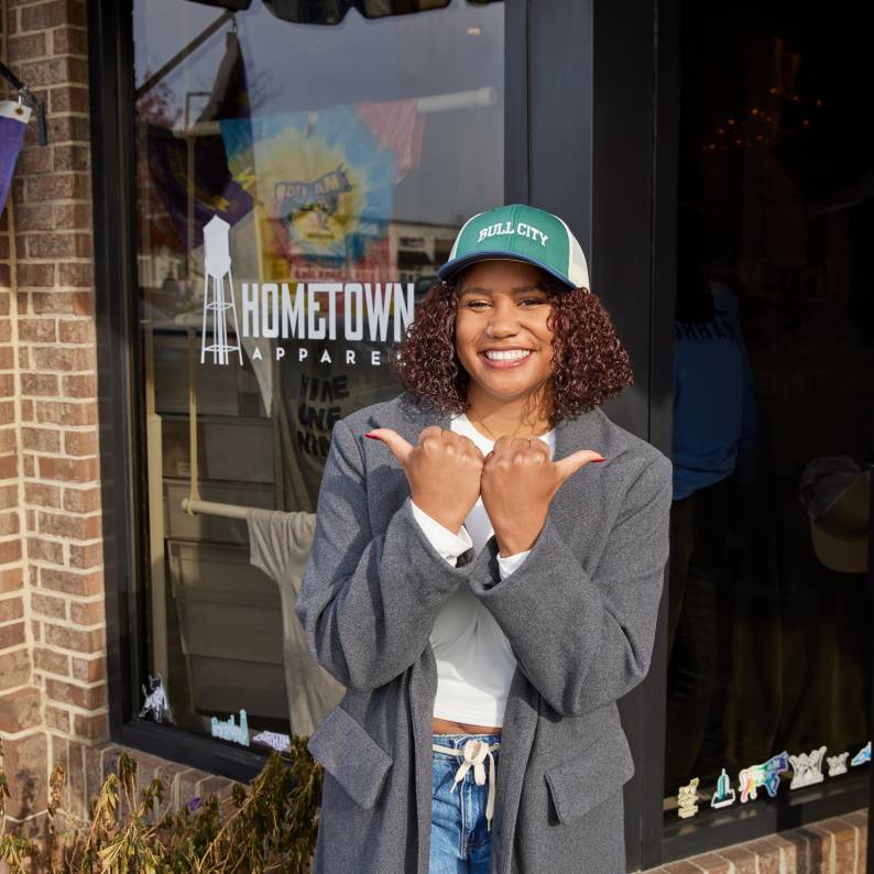 A shopper holds up their hands with the "Bull City" horns in front of Hometown Apparel in Durham, NC.