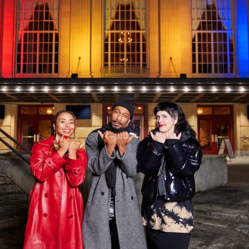 People pose outside The Carolina Theatre, featuring a light display showcasing the city of Durham's flag colors on the facade