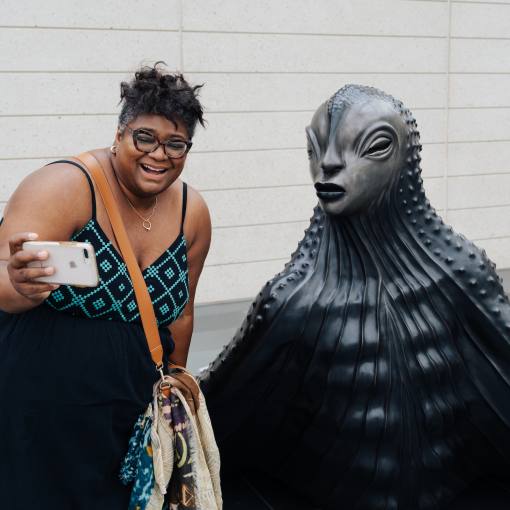 A woman takes a selfie next to a statue at The Nasher Museum of Art in Durham, NC.