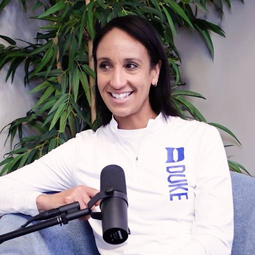 Duke Athletics Director Nina King sits in a blue chair in front of a plant with a podcast microphone in front of her.