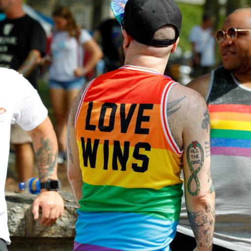 A pride parade goer wearing a "love wins" rainbow tanktop laughs with others at the parade.