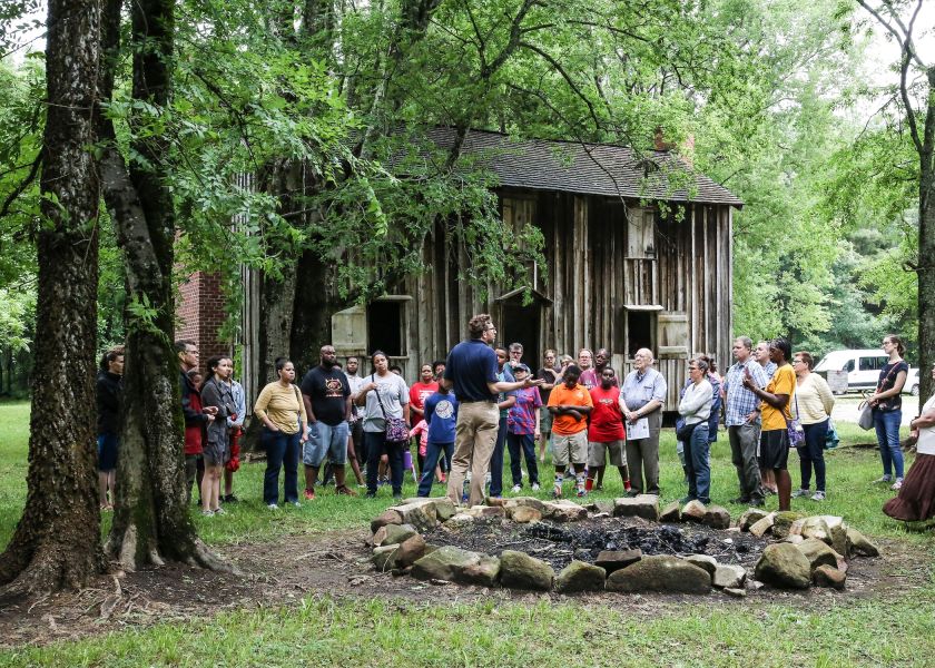 Visitors to Historic Stagville gather around on Juneteenth to hear a tour guide speak.