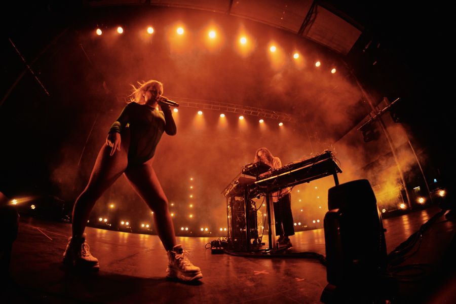 Amelia Meath stands on the stage performing under warm lighting.