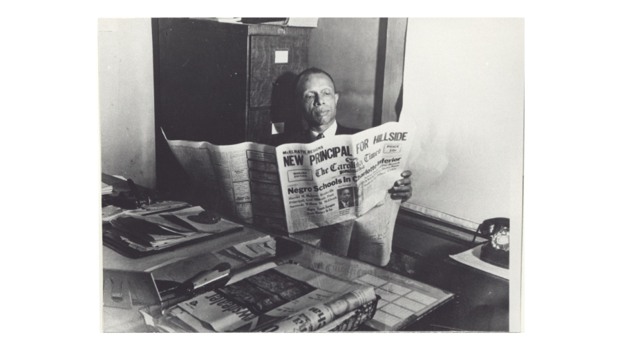 Journalist Louis Austin sits at his desk reading a newspaper in a black and white photo.